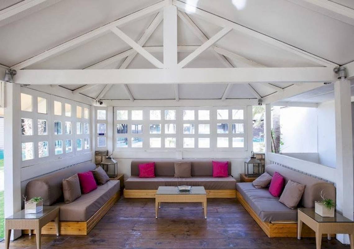 Innenbereich des Oasis Belorizonte Hotels mit weißen Wänden und Holzböden, mehrere Sofas mit Kissen und Tischen.