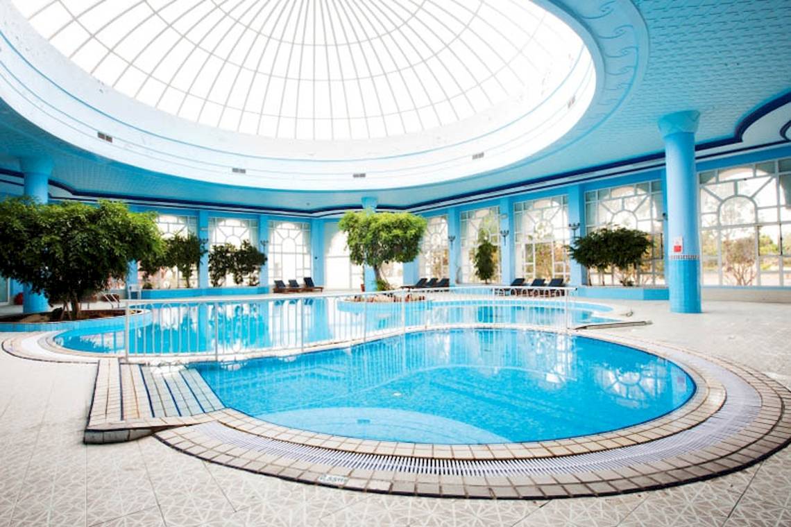 Innenpool des El Mouradi Djerba Menzel Hotels mit blauen Säulen und Glasdach
