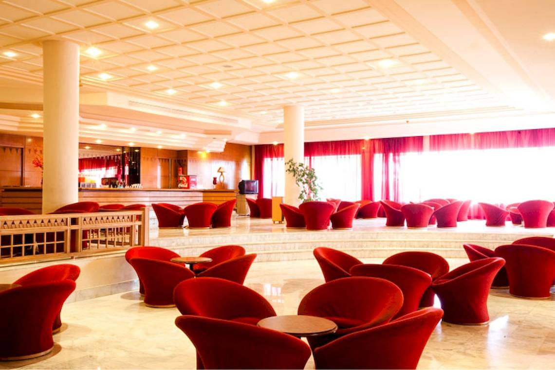 Innenbereich des El Mouradi Djerba Menzel Hotels mit roten Stühlen und einem Empfangstresen.