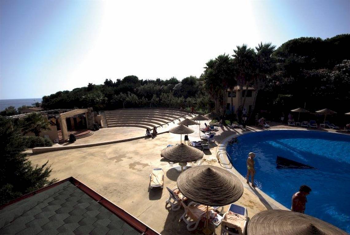 Oberansicht des TH Le Castella - Baia degli Dei Village mit Pool, Liegestühlen und Sonnenschirmen.
