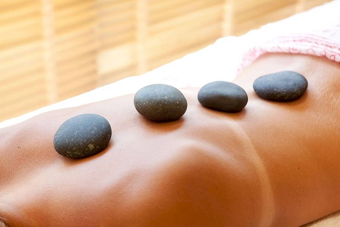 Massage mit Steinen auf dem Ruecken eines Menschen, vier Steine sind auf der Haut platziert.