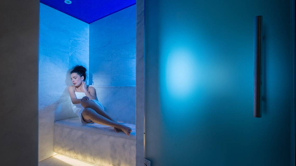 Eine Frau sitzt entspannt in einer blau beleuchteten Sauna im Silva Beach Hotel.