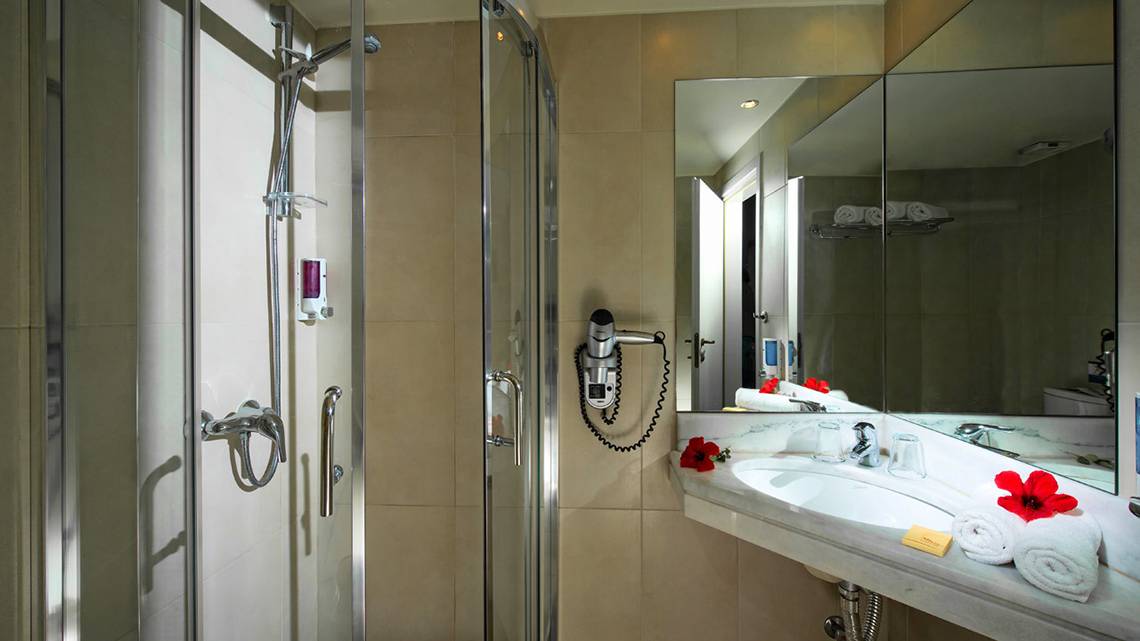 Badezimmer im Silva Beach Hotel mit Glasdusche, Handtuchtrockner und Spiegel.