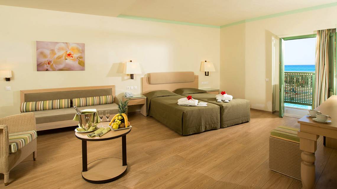 Doppelzimmer im Silva Beach Hotel mit Meerblick, zwei Betten, Tisch mit Früchten, Sofa und Balkon.