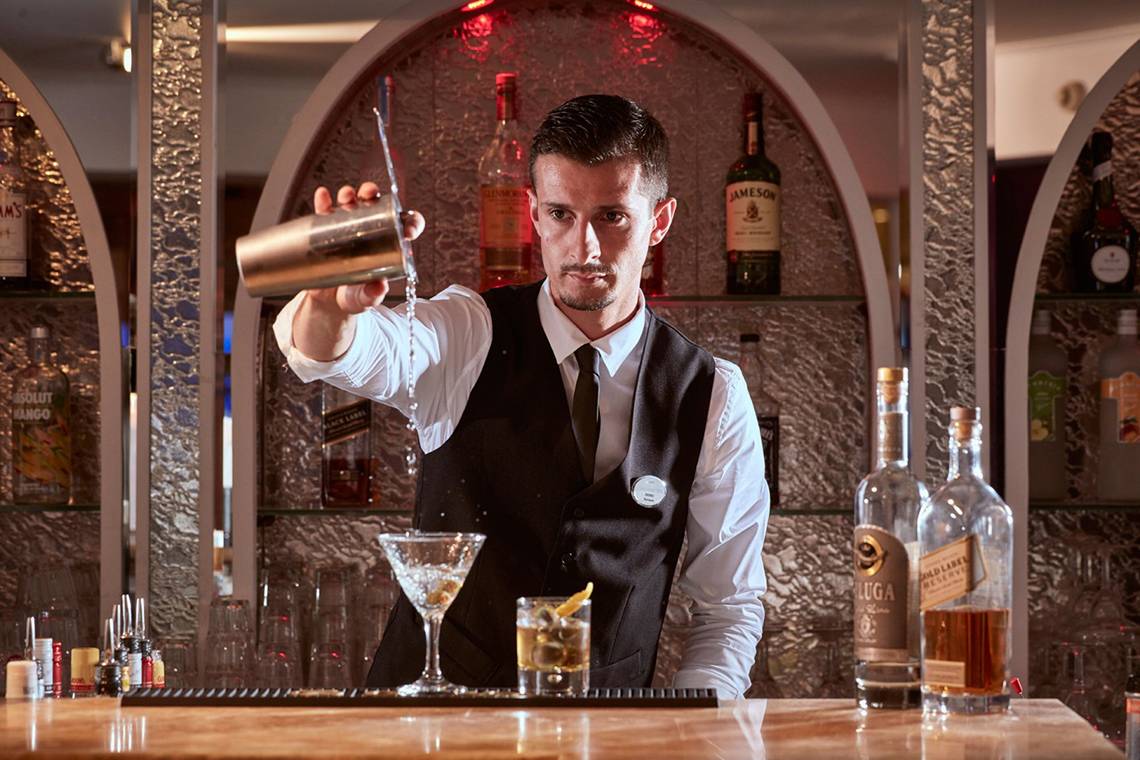 Ein Barkeeper im Grecian Park Hotel gießt einen Cocktail in ein Glas.