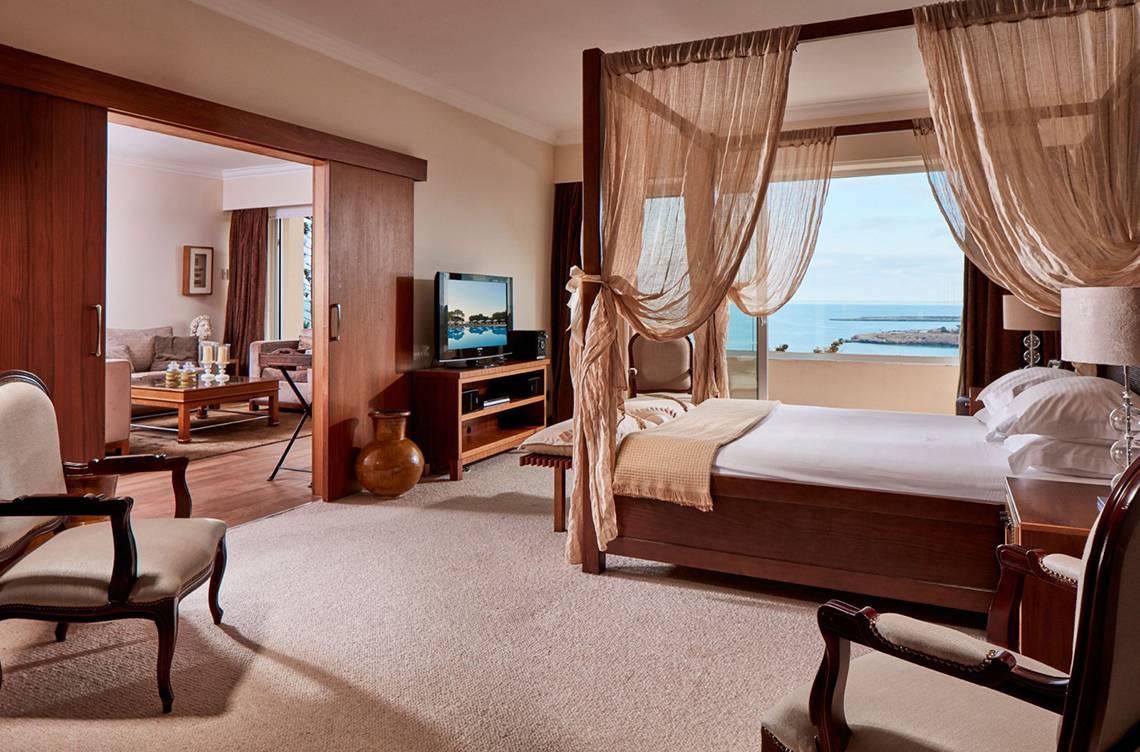 Schlafzimmer im Grecian Park Hotel mit Himmelbett, Fernseher und Meerblick.