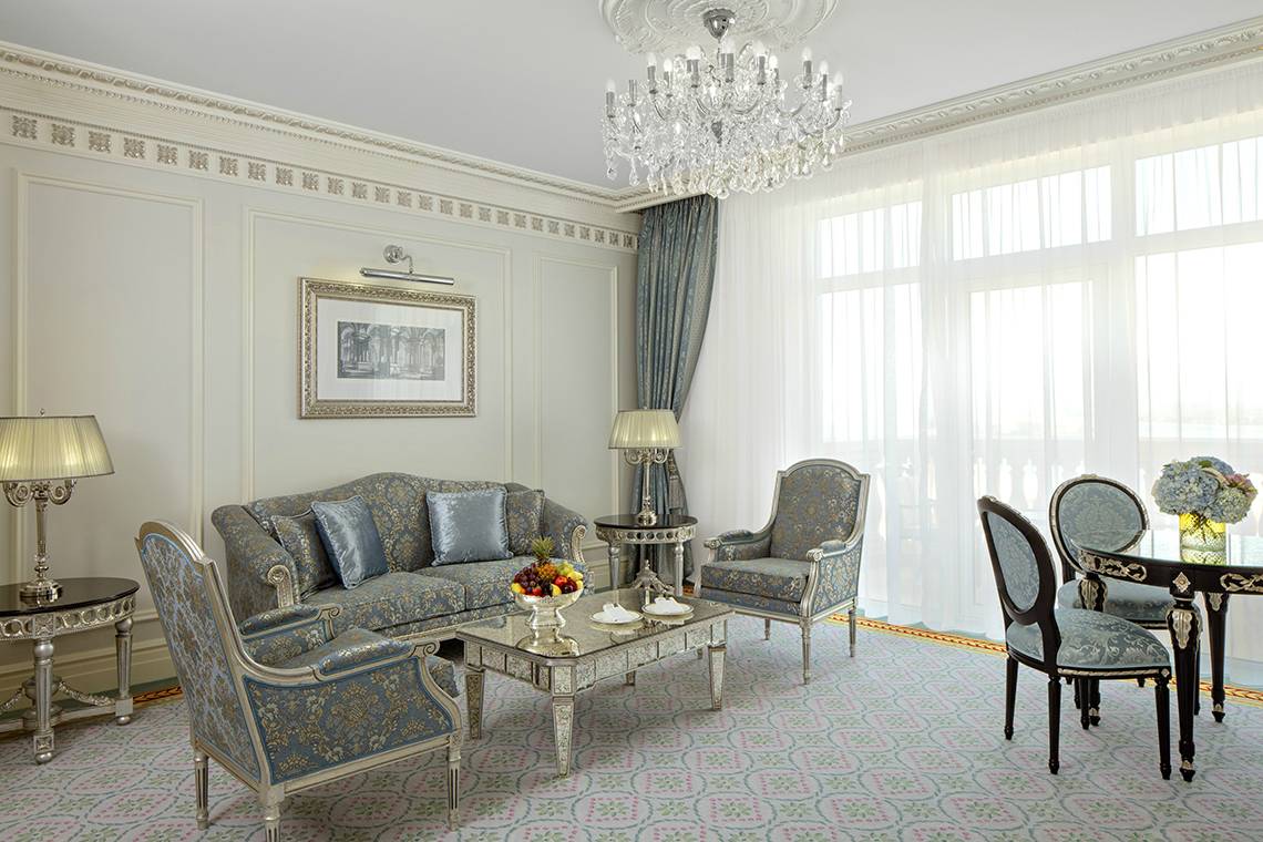 Wohnzimmer im Raffles The Palm Dubai Hotel mit Kristallkronleuchter, Sofa und Esstisch.