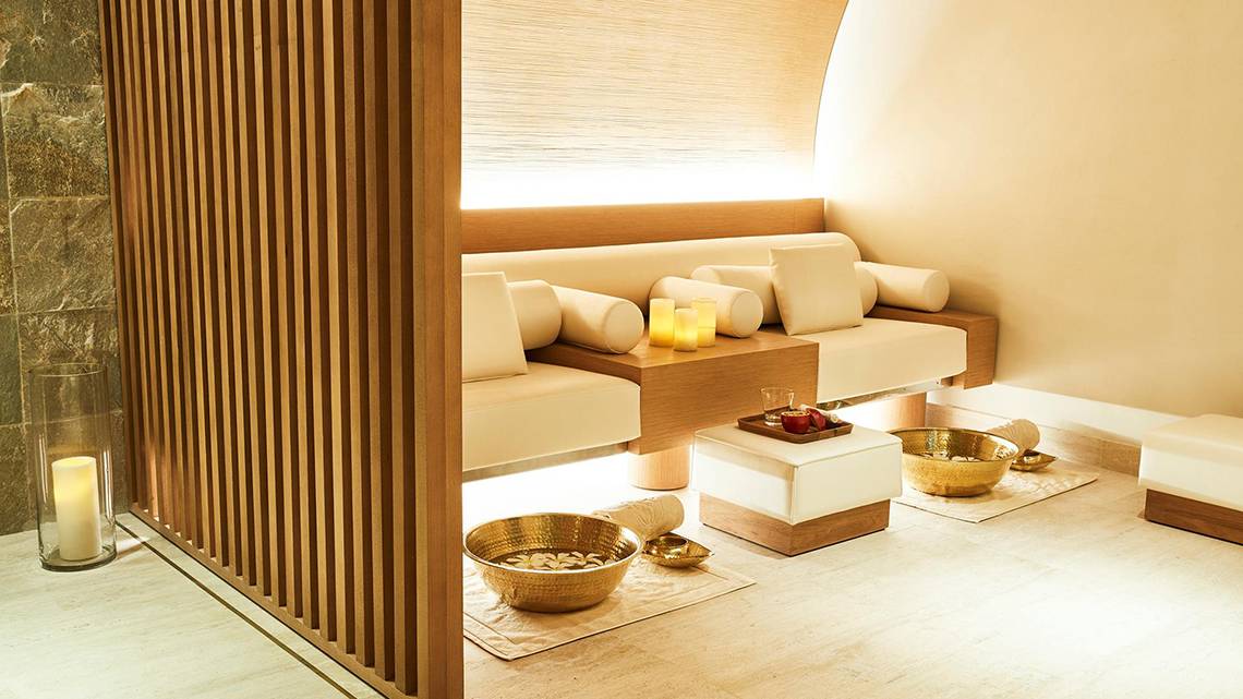 Spa-Behandlungsraum im Raffles The Palm Dubai mit weißen Möbeln, Holzelementen und Kerzen.