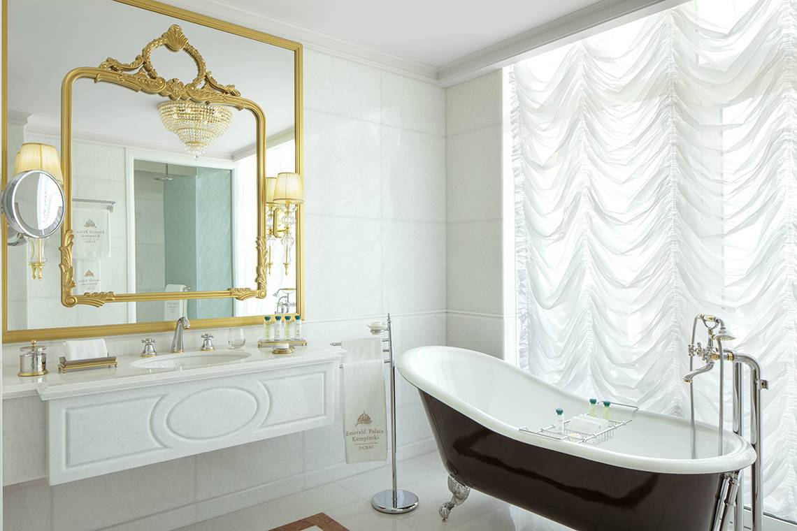 Badezimmer im Raffles The Palm Dubai mit goldenem Spiegel, Badewanne und Waschbecken.