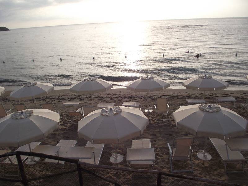 Ein Blick auf den Strand von Baia Di Nora mit vielen Sonnenschirmen und Liegen am Meer.