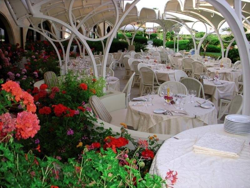 Außenbereich des Baia Di Nora Restaurants mit gedeckten Tischen und farbenfrohen Blumen.