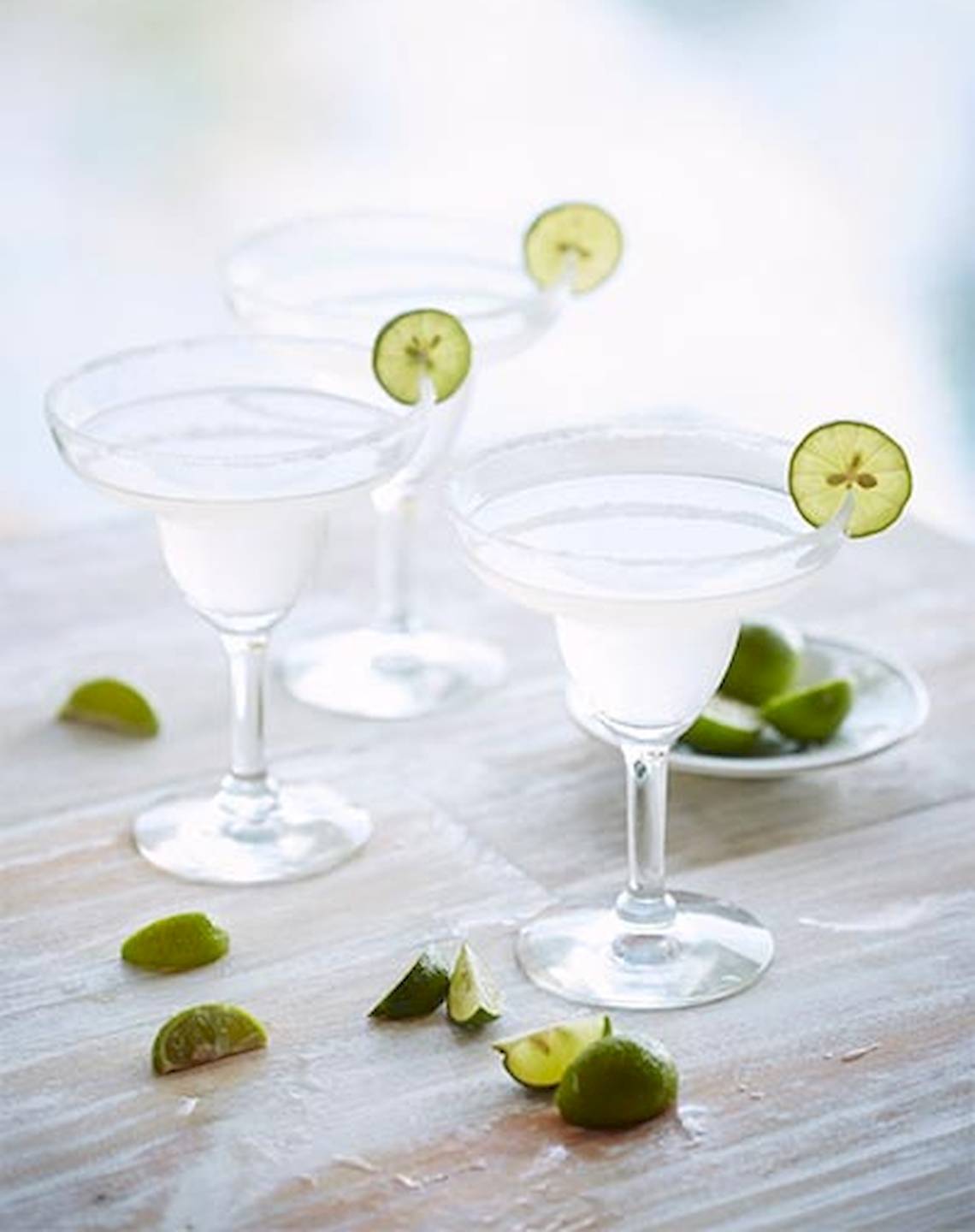 Drei Cocktails mit Limettenscheiben auf einem Holztisch.