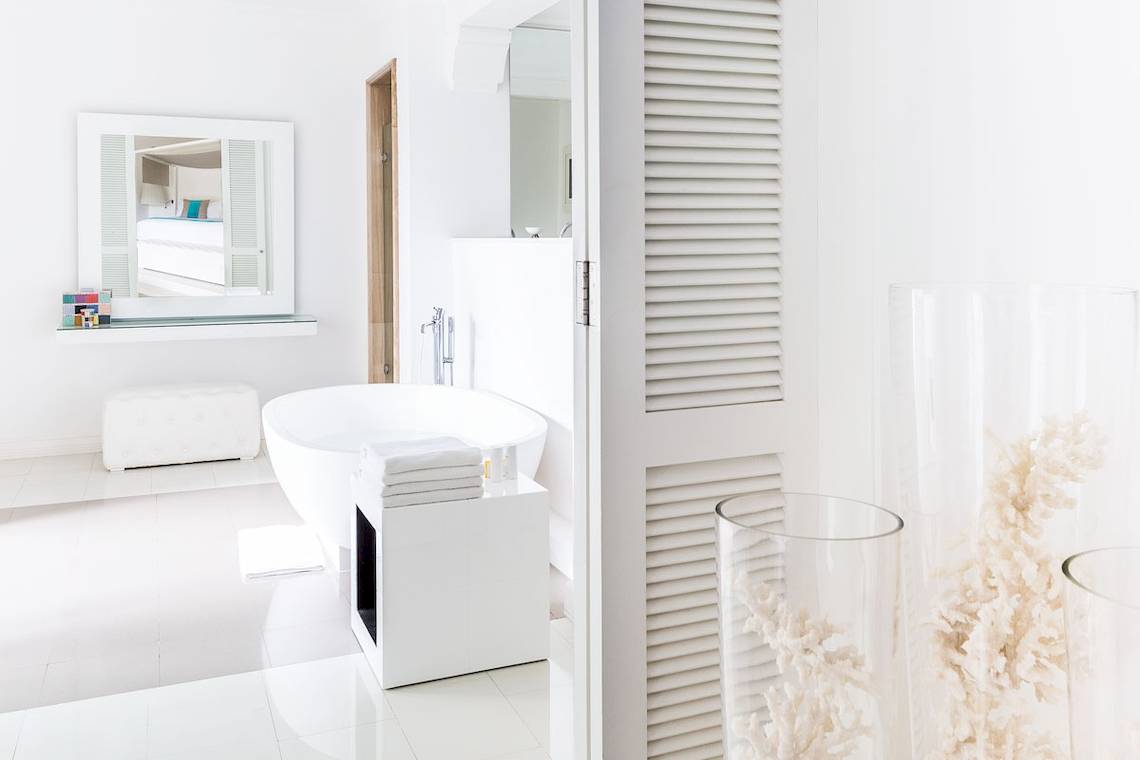 Das Badezimmer des LUX Belle Mare Resort & Villas mit einer weißen Badewanne, Spiegel und weißen Möbeln.