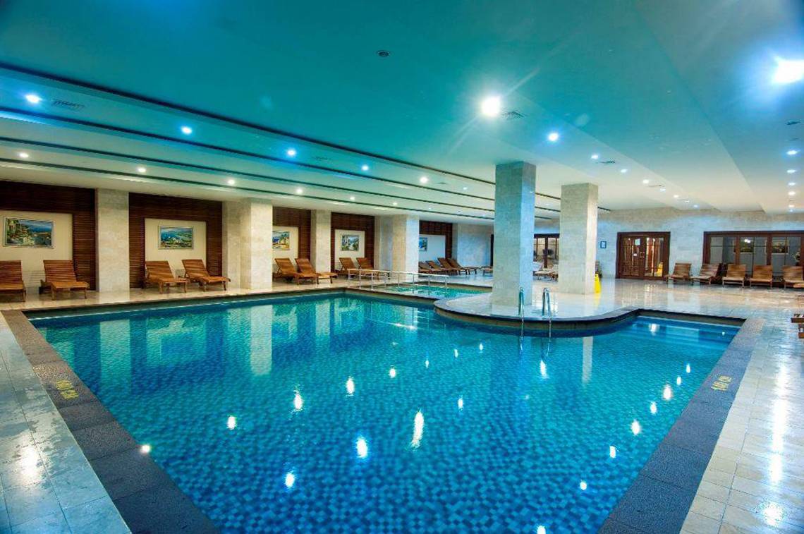 Innenpool des Orange County Belek - Family Concept Hotels mit blauen Fliesen und Lounge-Stühlen.