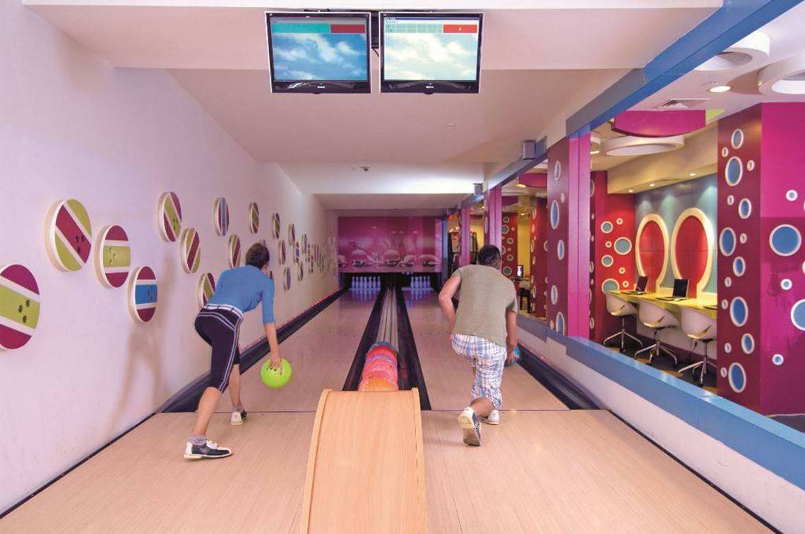 Zwei Leute bowlen in einer Halle mit bunten Wänden und Bowlingbahnen.
