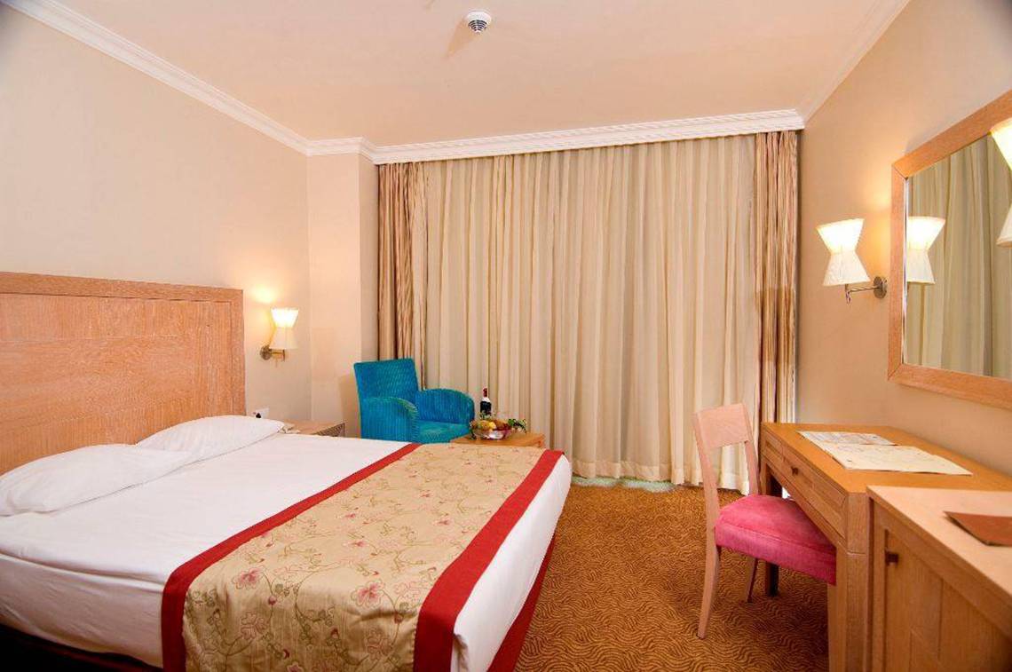 Hotelzimmer im Orange County Belek Family Concept mit Doppelbett, blauem Stuhl und Schreibtisch.