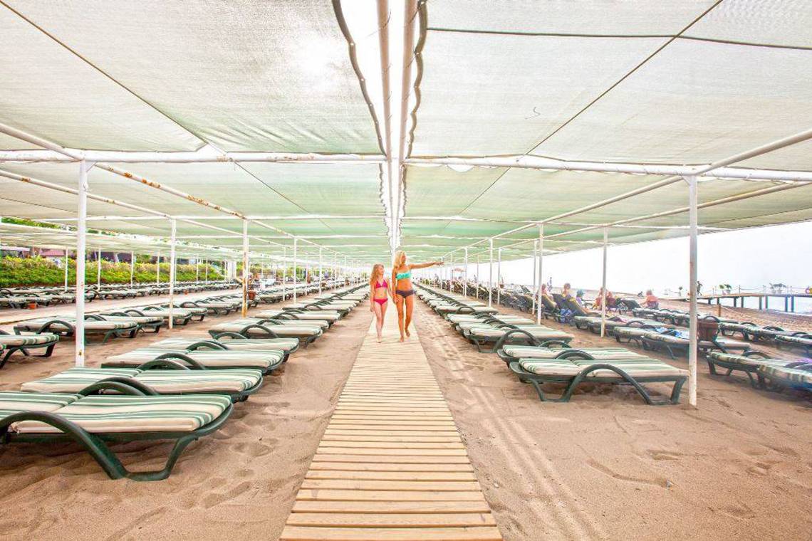 Zwei Frauen gehen auf einem Holzsteg zwischen Strandliegen des Orange County Belek - Family Concept
