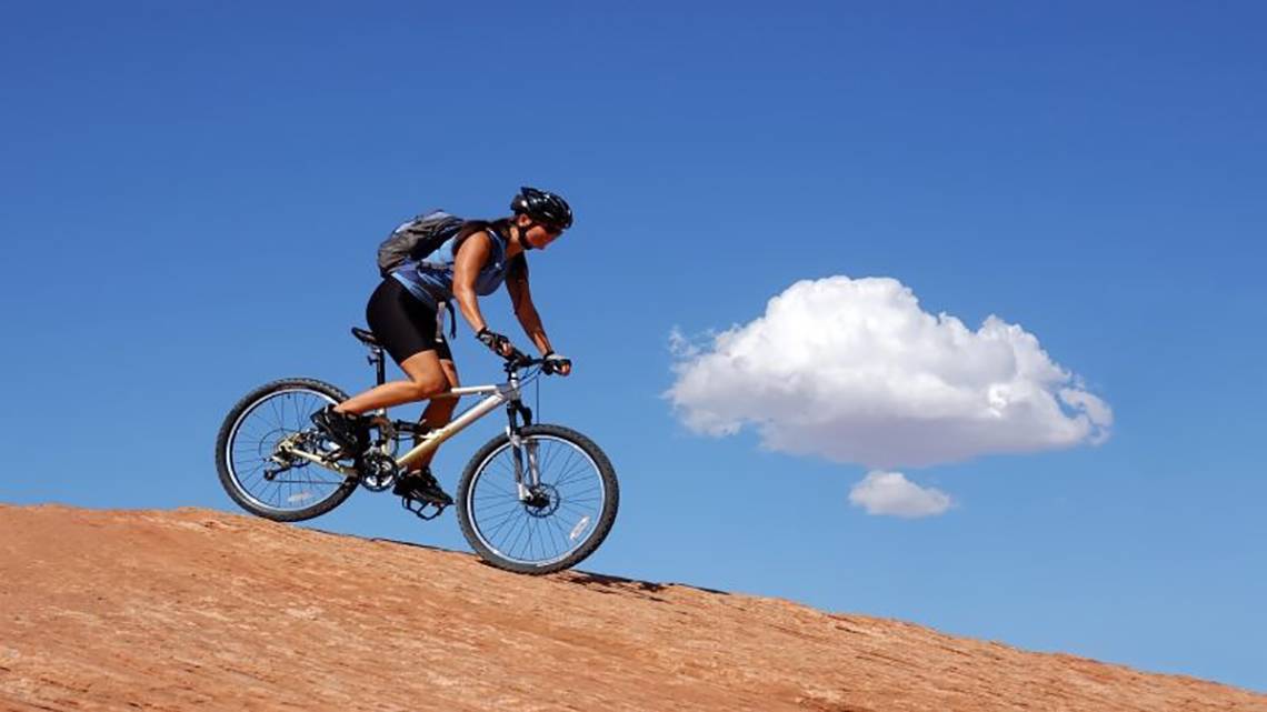 Frau mit Fahrrad auf einem Berg, im Himmel ist eine Wolke sichtbar