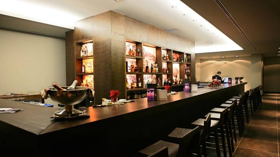 Bar im Barcelo Tenerife Hotel mit Tresen, Flaschen und Stühlen.