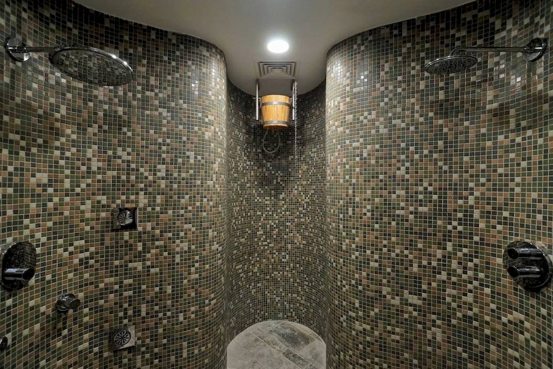 Eine geflieste Dusche im Melissi Beach Hotel & Spa mit zwei Duschköpfen und einer Holzeimer.