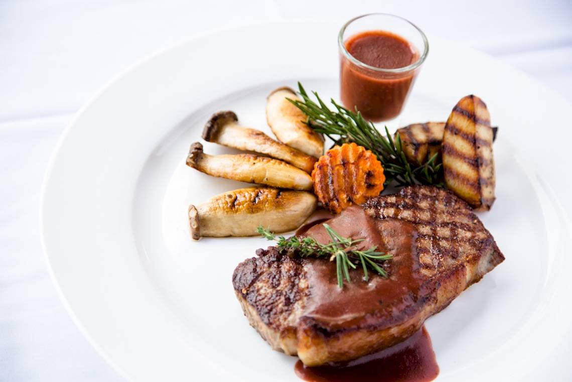 Gegrilltes Steak mit Sauce und Gemüse auf einem weißen Teller serviert.
