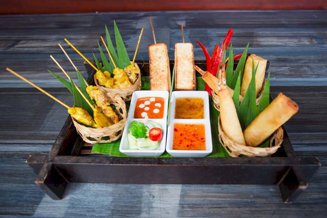 Thailändisches Gericht auf einer Holzplatte mit verschiedenen Fleischspießen und Beilagen.