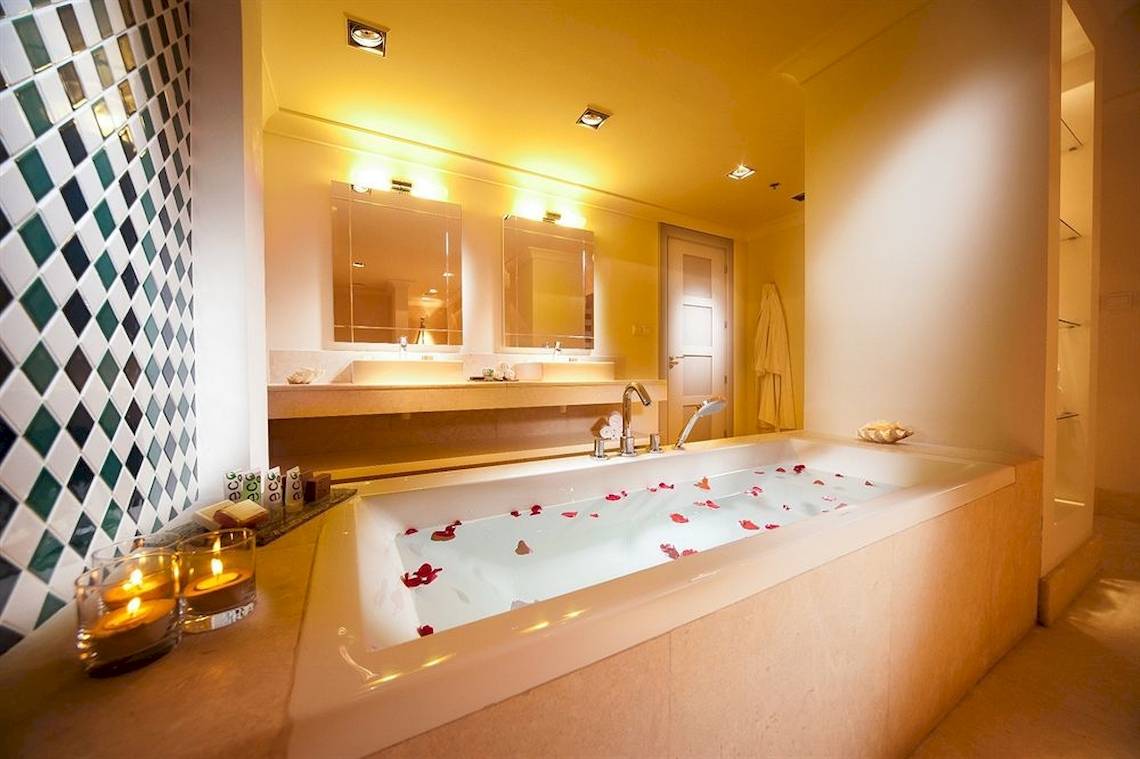 Badezimmer im Juweira Boutique Hotel mit Badewanne, Kerzen und Rosenblättern.