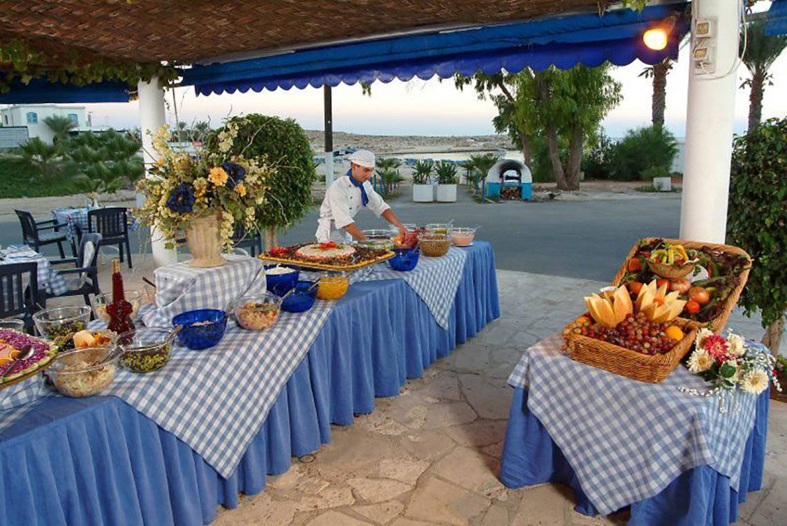 Ein Koch bereitet ein Buffet auf dem Tisch des Anonymous Beach Hotels vor, mit verschiedenen Gerichten und Früchten.