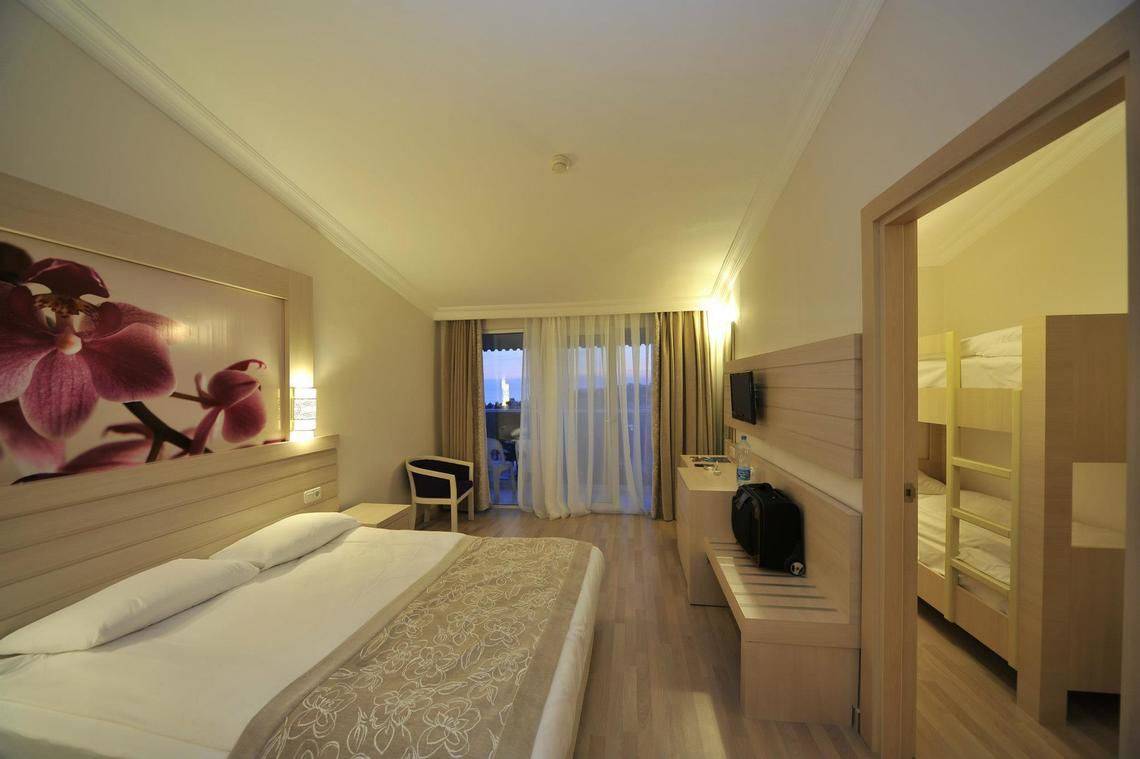 Innenansicht eines Zimmers im Seaden Corolla Hotel mit Doppelbett, Nachttisch, Fernseher und Balkon.