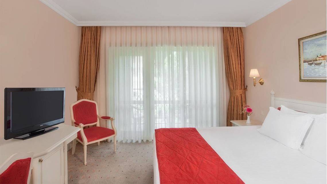 Innenansicht eines Hotelzimmers im Kremlin Palace Hotel mit Fernseher, Bett und Stuhl.