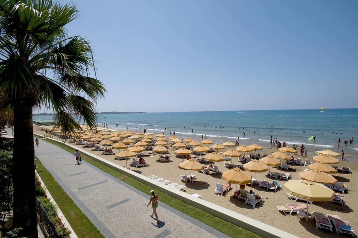 Strand mit vielen Sonnenschirmen und Liegestühlen, Palme und Spazierweg, Menschen schwimmen im Meer