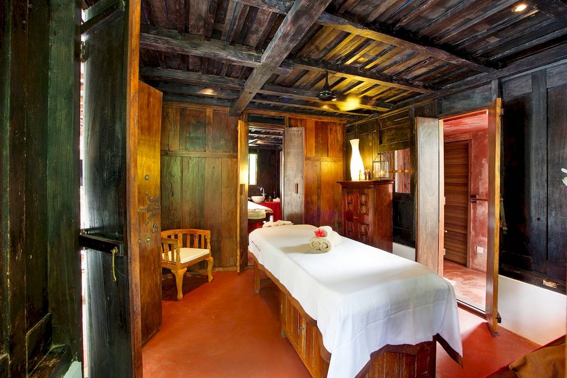 Massageraum im Gangehi Island Resort mit Behandlungstisch und Holzmöbeln.