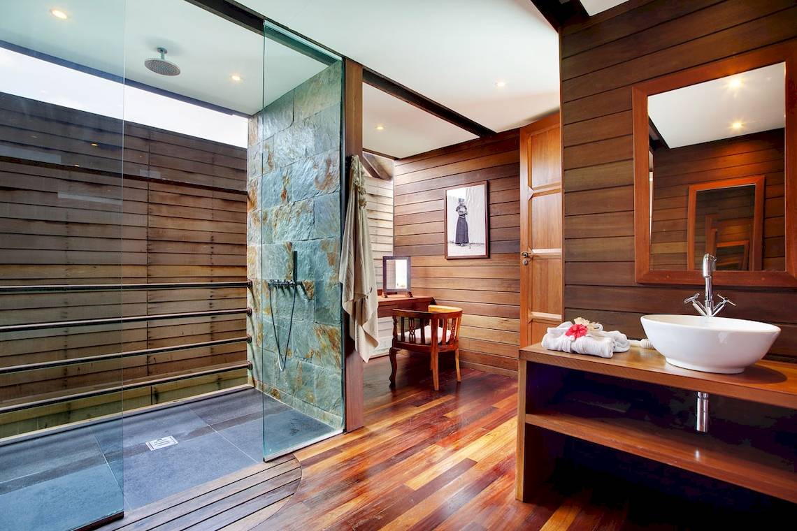 Innenansicht des Badezimmers im Gangehi Island Resort mit Glasdusche, Holzwänden und Möbeln.