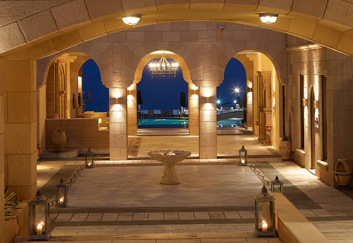 Der gepflasterte Eingangsbereich des Mitsis Lindos Memories Resort & Spa mit beleuchteten Laternen und einem Brunnen.