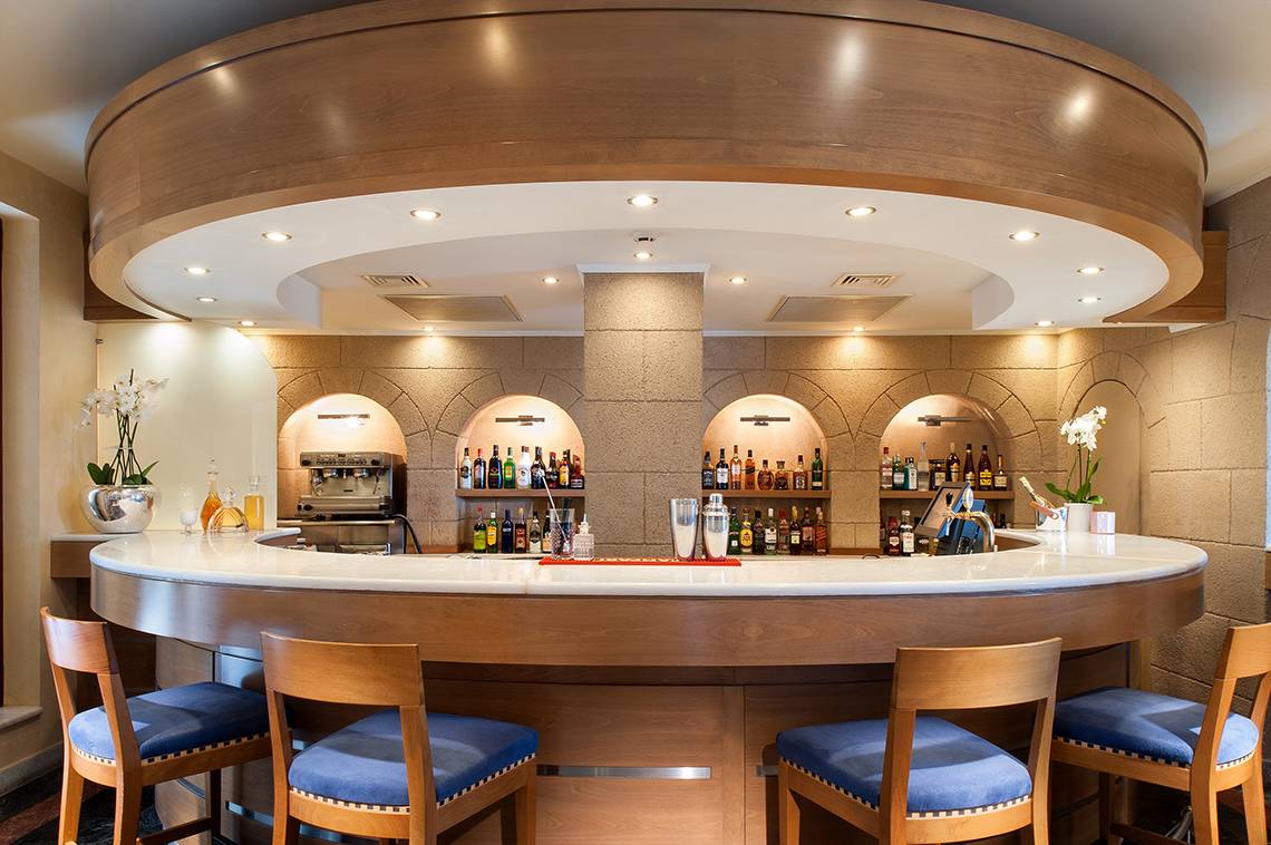 Bar im Mitsis Lindos Memories Resort & Spa mit Holzmöbeln und Getränken.