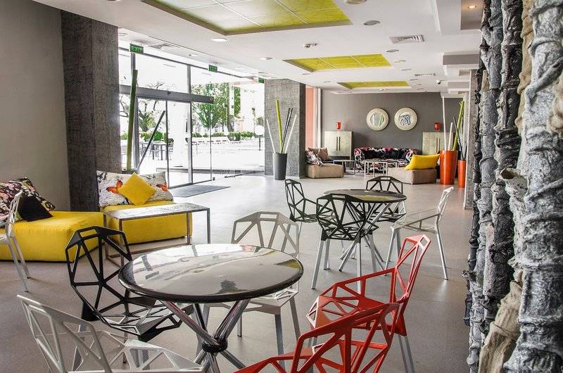 Lobbybereich des Gladiola Star Hotels mit bunten Stühlen und Tischen, gelben Sofas und einer Steinmauer.