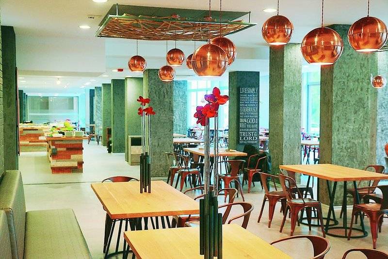 Innenbereich des Gladiola Star Hotels mit runden Kupferlampen und grünen Säulen.