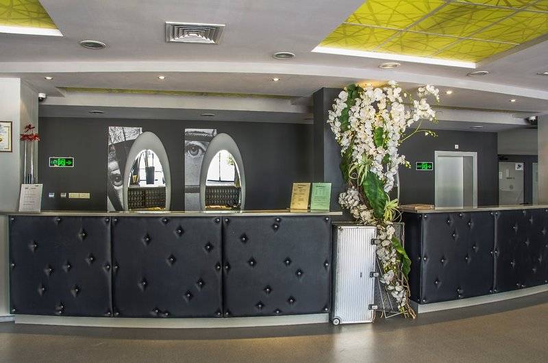 Innenansicht der Rezeption im Gladiola Star Hotel mit schwarzem gepolsterten Tresen, weißen Blumen und moderner Gestaltung.