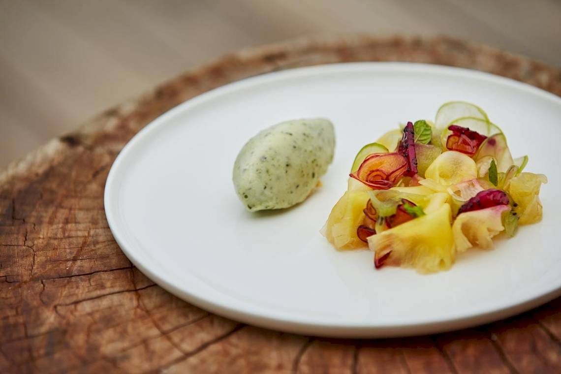 Gerecht auf einem weißen Teller, umgeben von einem grünen Eisball, serviert auf einem Holzbrett im LUX Grand Gaube Resort & Villas.