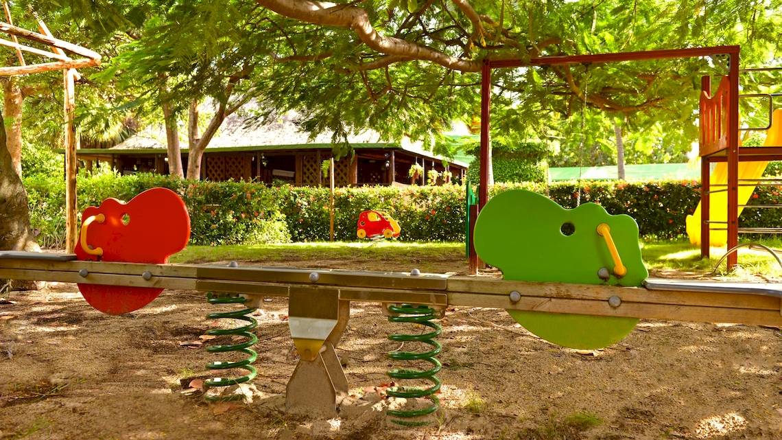 Kinderspielplatz im Garten des Iberostar Tainos Hotels mit bunten Spielgeräten und Bäumen.