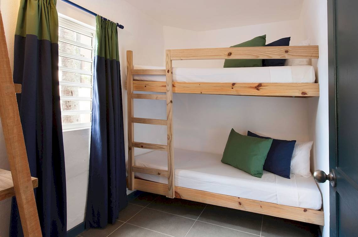 Doppel-Stockbett im Zimmer des Veranda Pointe Aux Biches Hotels mit grünen und blauen Kissen und weißen Laken.