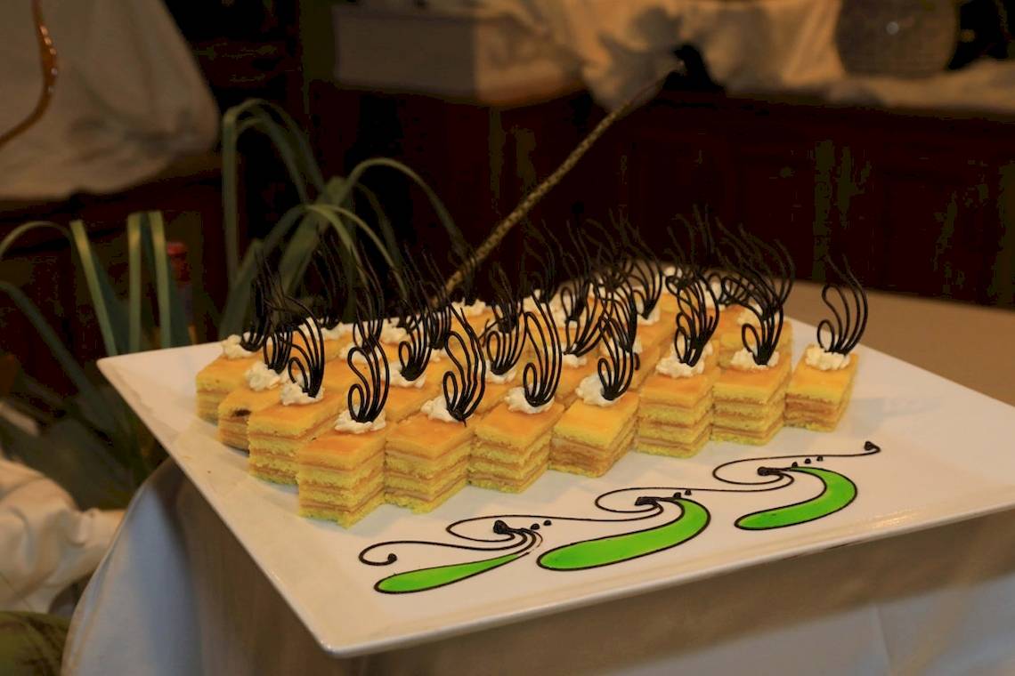 Foto von einem weißen Teller mit mehreren Stücken Kuchen gefüllt mit einer gelben Creme und schwarzen Dekorationen.