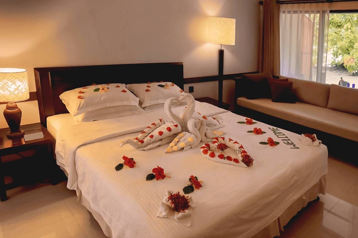 Doppelbett mit Blumen und Entspannungs-Dekor im Hotelzimmer