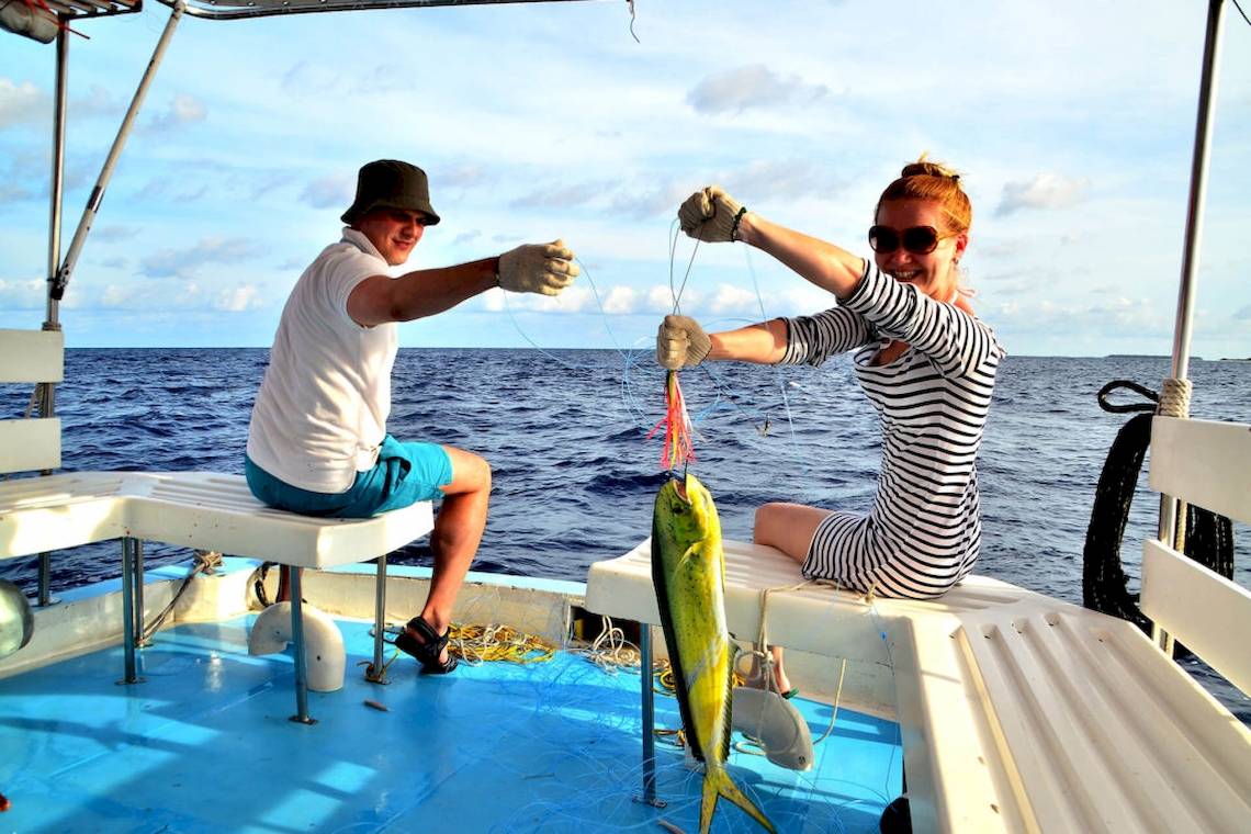 Zwei Personen auf einem Boot, die einen Fisch fangen, vor dem Hintergrund des Villa Park Hotels in den Malediven.