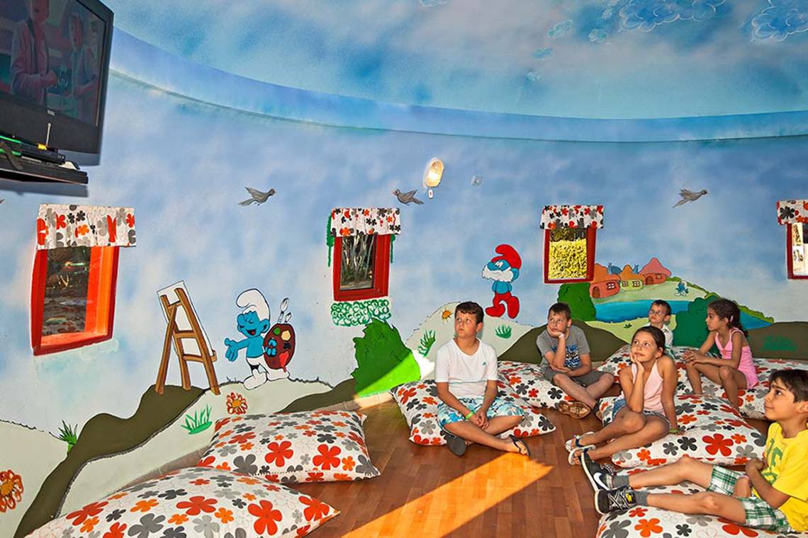 Kinderzimmer mit Schlumpfisch-Wandmalerei und Kindern, die auf Kissen sitzen.