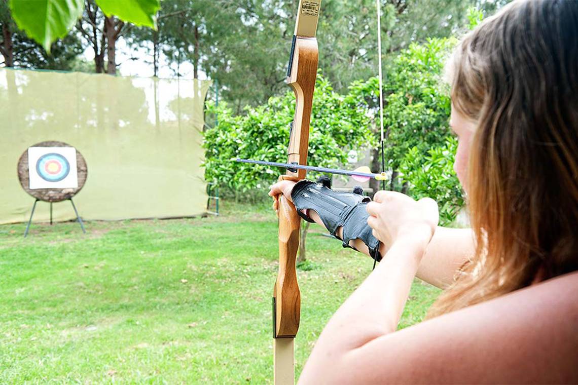 Frau schießt mit einem Bogen im Garten auf eine Zielscheibe.