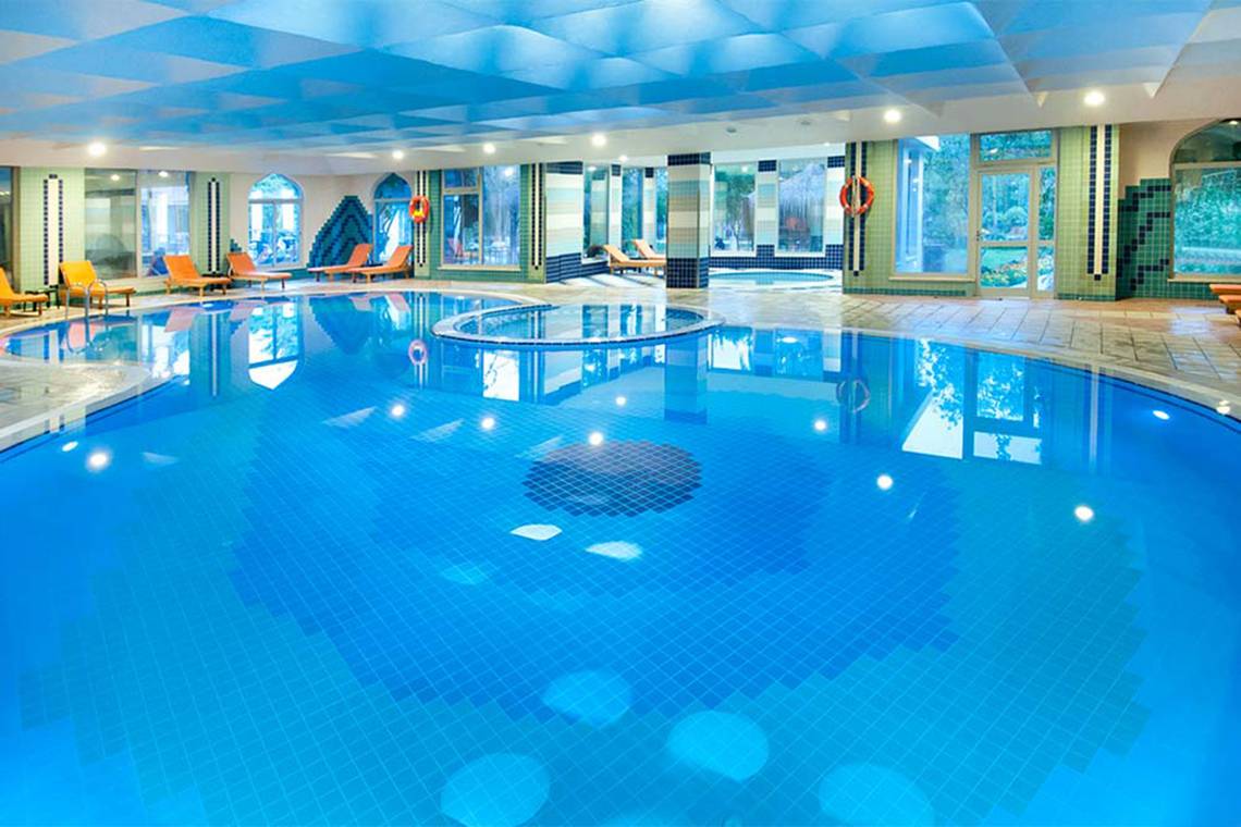 Innenpool des Belconti Resorts mit blauen Fliesen und Lounge-Bereichen.