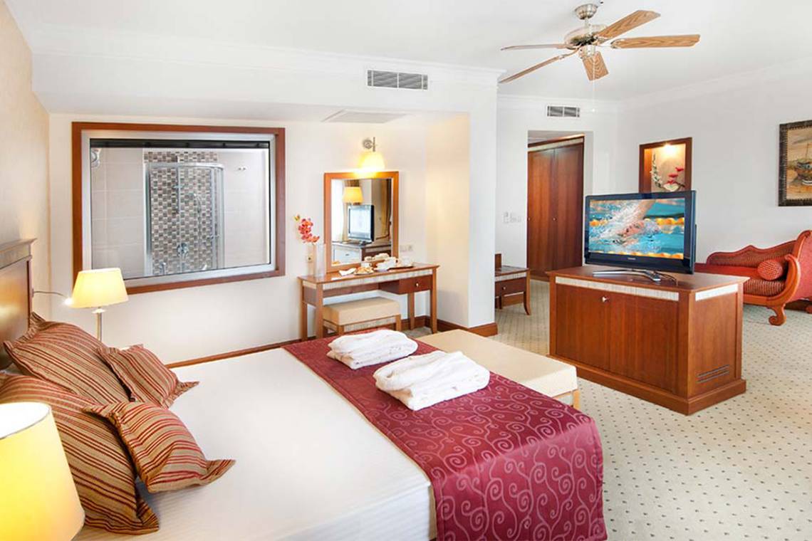 Innenansicht eines Hotelzimmers im Belconti Resort mit Bett, Fernseher, Schreibtisch und Dusche.