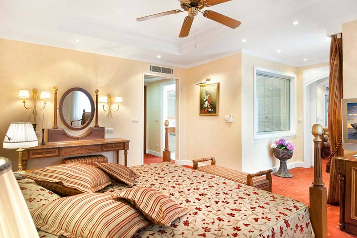 Ein elegantes Schlafzimmer im Belconti Resort mit einem großen Bett, einem Spiegel, einem Schreibtisch und einer Deckenventilator.
