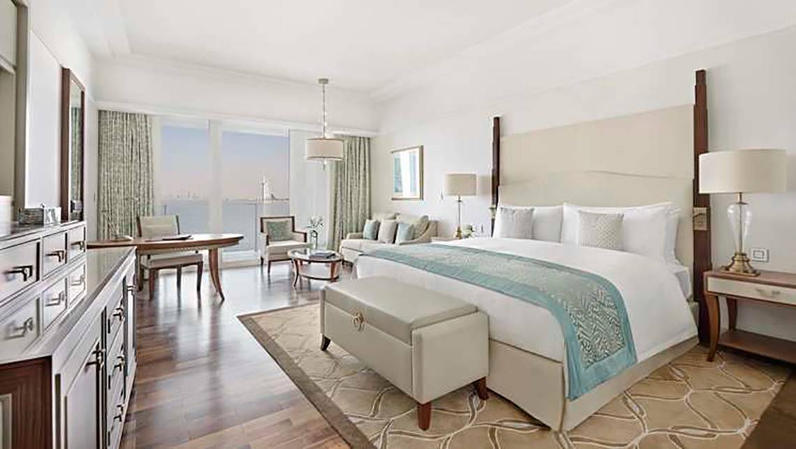 Innenansicht einer Suite im Waldorf Astoria Dubai Palm Jumeirah mit großem Bett, Schreibtisch und Blick auf das Meer.
